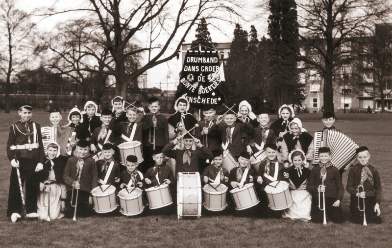 Stadsmatenstraat Kinderen van drumband en dansgroep Bonte Boertjes met instrumenten en in klederdracht in het Volkspark. Op de achtergrond het Wilhelminaflat.jpg