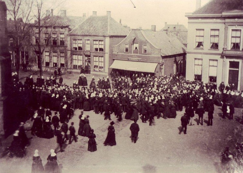 Markt het uitgaan van de Grote Kerk in 1893 met linomadefabriek Barske (nu Poort van Kleef) en slager Menco later manufacturenhandel De Zon en weer later cafe Monopool.jpg