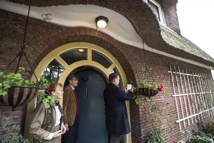 Wethouder Diepemaat bevestigt het monumentenbordje bij de voordeur van villa De Keizer, onder het toeziend oog van de bewoners, het echtpaar Gaymans.jpg