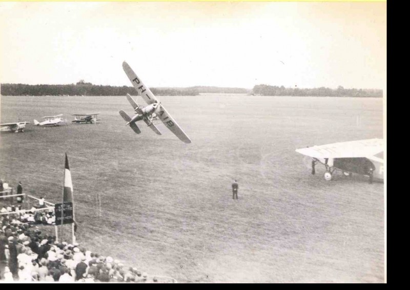 Vliegveldweg 1932 Vliegfeest met vliegtuig in de lucht en enkele vliegtuigen van het type PH-AEB en PH-AIB die op grond staan.jpg