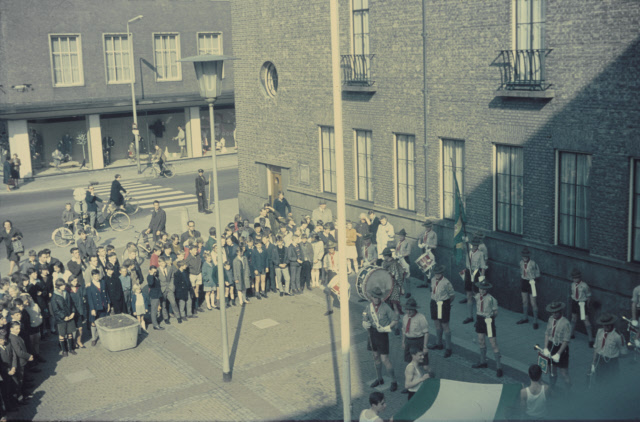 Langestraat 24 Leden van sportvereniging hijsenstrijken groen-wit-groene vlag op plein voor stadhuis, in het bijzijn van publiek en padvinders drumband. jaren 70.jpeg