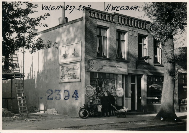 Haaksbergerstraat 306-308 Dubbel winkel-woonhuis (voor en zijkant) met dames die etalage bekijken bij een winkel van sinkel bord Hier het Wonder voor Twente o.a. reparatie  rijwielen stofzuigers strijkijzers. 1950.jpeg