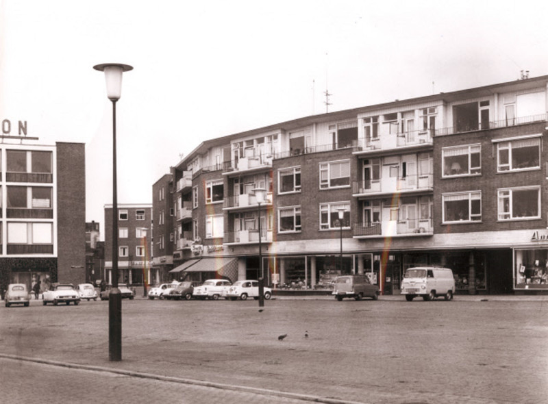 H.J. van Heekplein 26 met geparkeerde auto's, woningen en winkels, o.a. Anny Kaiser, Bakkerij Jagers Brood en Banket, Bastet. Links is de Hermes flat zichtbaar.jpeg